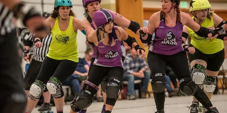 A pivot in purple skating with a striped helmet cover among blockers